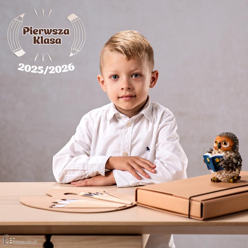Chłopak idący do pierwszej klasy siedzi przy biurku z paleta pędzli, teczką i sową